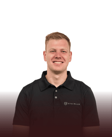 Man in zwart Stairlux uniform met logo, lachend, professionele uitstraling.