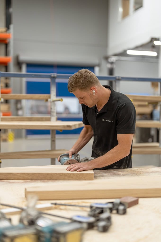 Houtsnijder bewerkt houten plank in showroom van Stairlux met professionele gereedschappen.